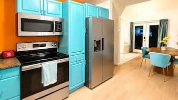 A modern kitchen with teal cabinets, a stainless steel microwave, and a refrigerator.