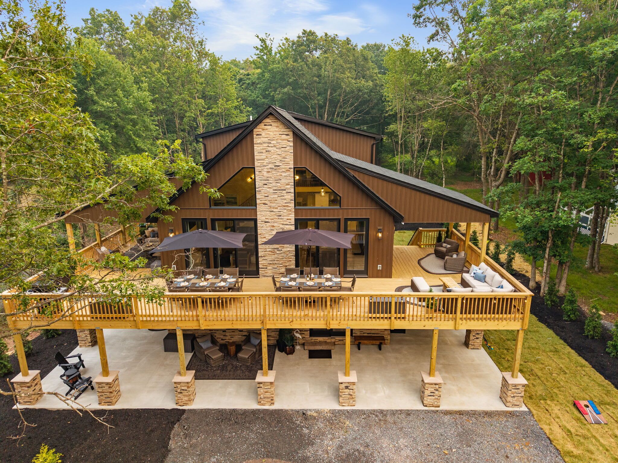 Une maison à deux étages avec une façade en pierre, un patio couvert avec des meubles d’extérieur et une terrasse dotée d’une balustrade.