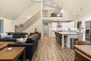 A spacious living area with a staircase, a kitchen with white cabinets, and a dining area with a wooden table. - Pool, Hot Tub, Sauna, Game Room, Luxury and More! (Albrightsville)