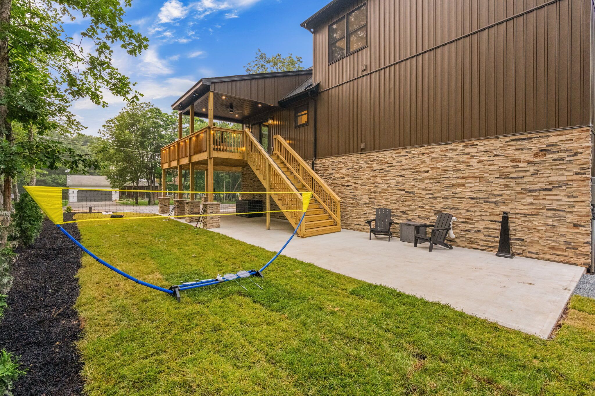A backyard with a wooden deck, a stone wall, and a concrete patio.