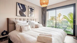 Camera d'albergo con un letto grande, un comodino, una finestra vista palme e opere d'arte alle pareti.