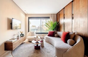 A modern living room with a sofa, a coffee table, a TV mounted on the wall, and a large window. - Cozy Studio in Central Casablanca (Casablanca)