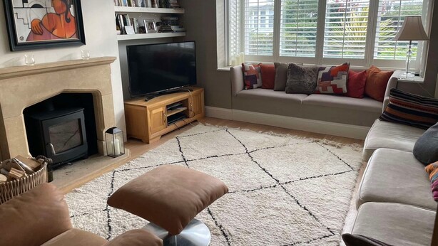 Ett vardagsrum med en öppen spis, en tv, en bokhylla och ett fönster med persienner.