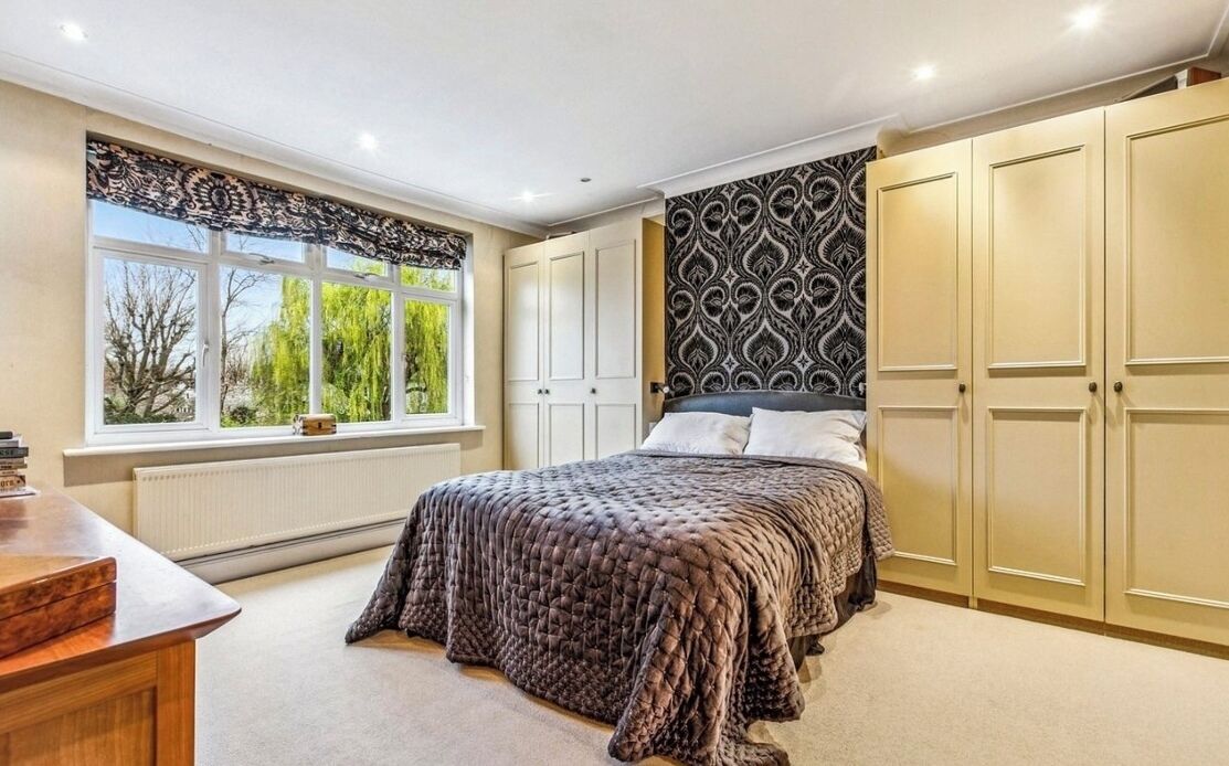 A bedroom with a bed, a window with curtains, a radiator, and a wardrobe.