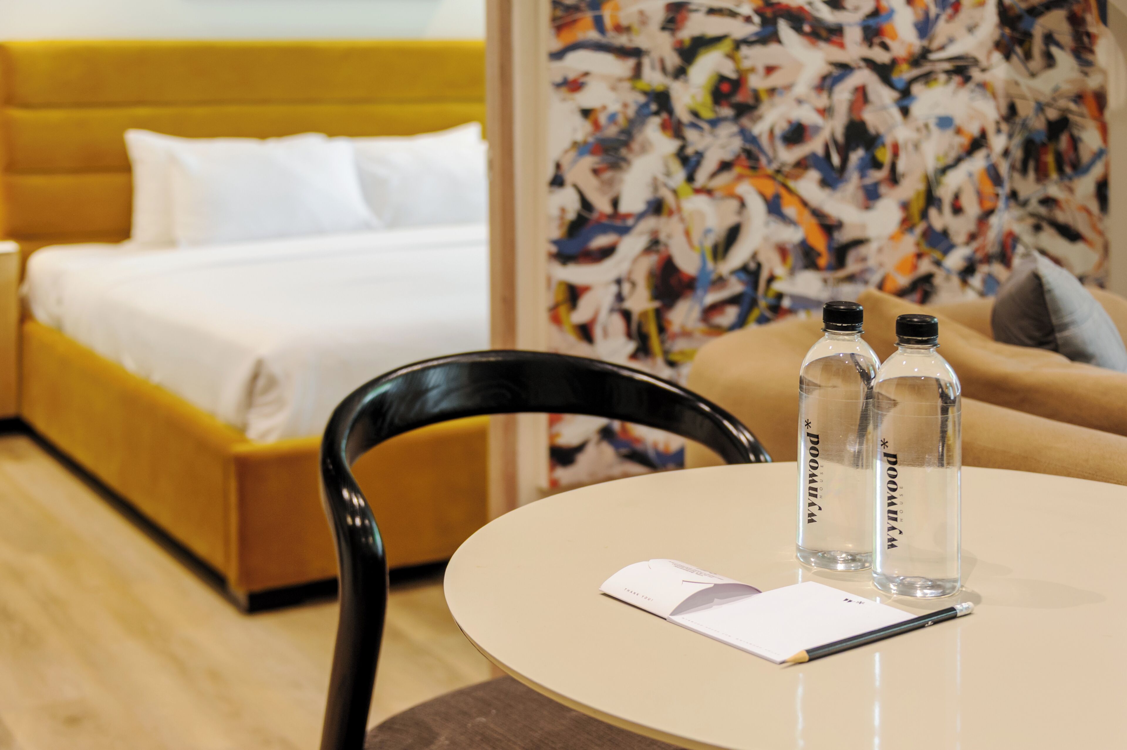 Una habitación de hotel con una cama, una mesa redonda, dos botellas de agua, una silla y un papel.
