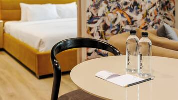 Una habitación de hotel con una cama, una mesa redonda, dos botellas de agua, una silla y un papel.