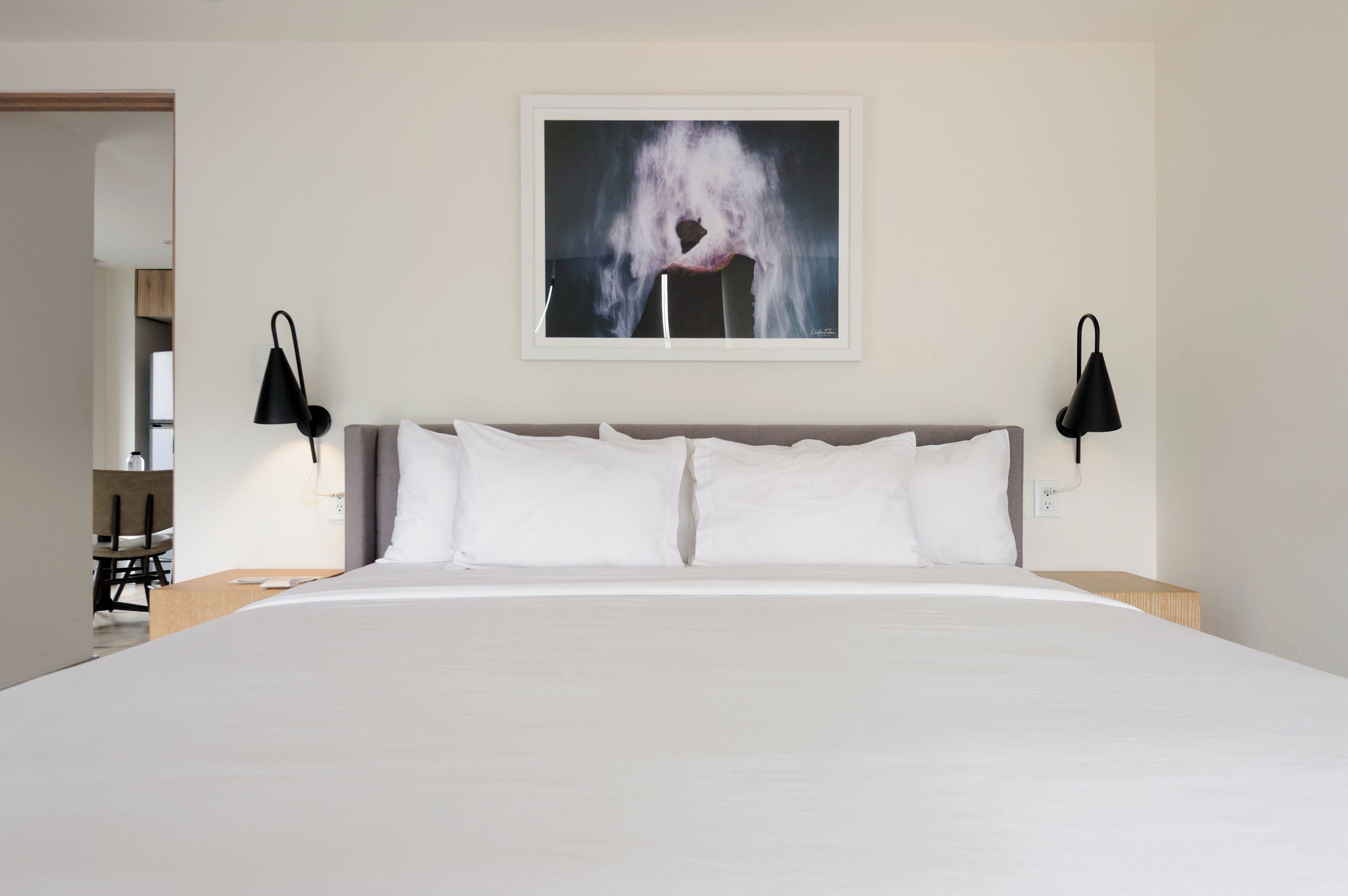A hotel room with a large bed, two black wall sconces, and a framed abstract painting above the bed.