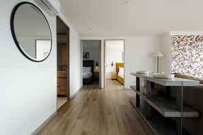 A modern hotel room with a wooden floor, a round mirror, a bed with a headboard, a bedside table with bowls, a sofa, and a lamp. - Rio Nazas 23 by Wynwood House (Ciudad de México)