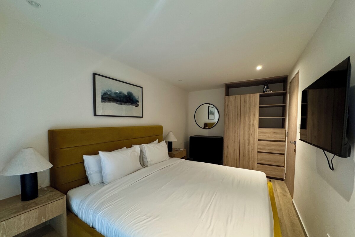 Une chambre à coucher avec un lit, des lampes de chevet, une télévision, une armoire et un tableau encadré au mur.