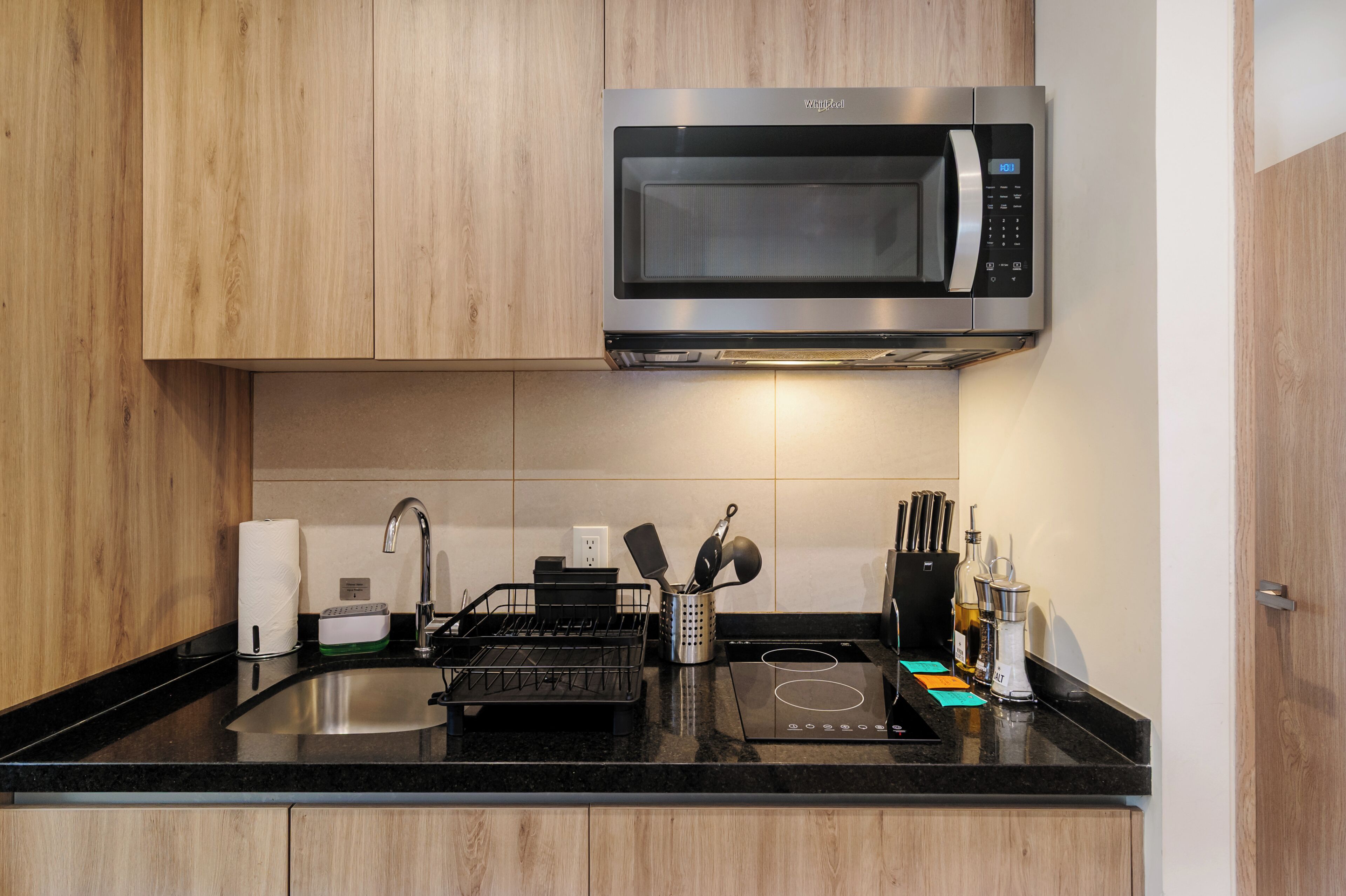 Una cocina moderna con microondas integrado, un lavabo con escurreplatos y una encimera con diversos utensilios de cocina.