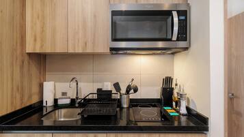 Una cocina moderna con microondas integrado, un lavabo con escurreplatos y una encimera con diversos utensilios de cocina.