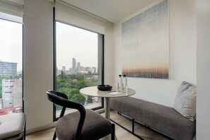 Una habitación moderna con un ventanal grande, una mesa redonda, una silla negra, un sofá gris y vistas a la ciudad.