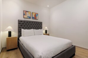 Una cama bien hecha con un cabecero capitonado, dos lámparas de noche y dos cuadros abstractos en la pared.