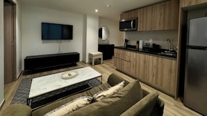 A modern living room with a sofa, a coffee table, a TV, and a kitchen area with wooden cabinets and a refrigerator. - Rio Nazas 23 by Wynwood House (Ciudad de México)