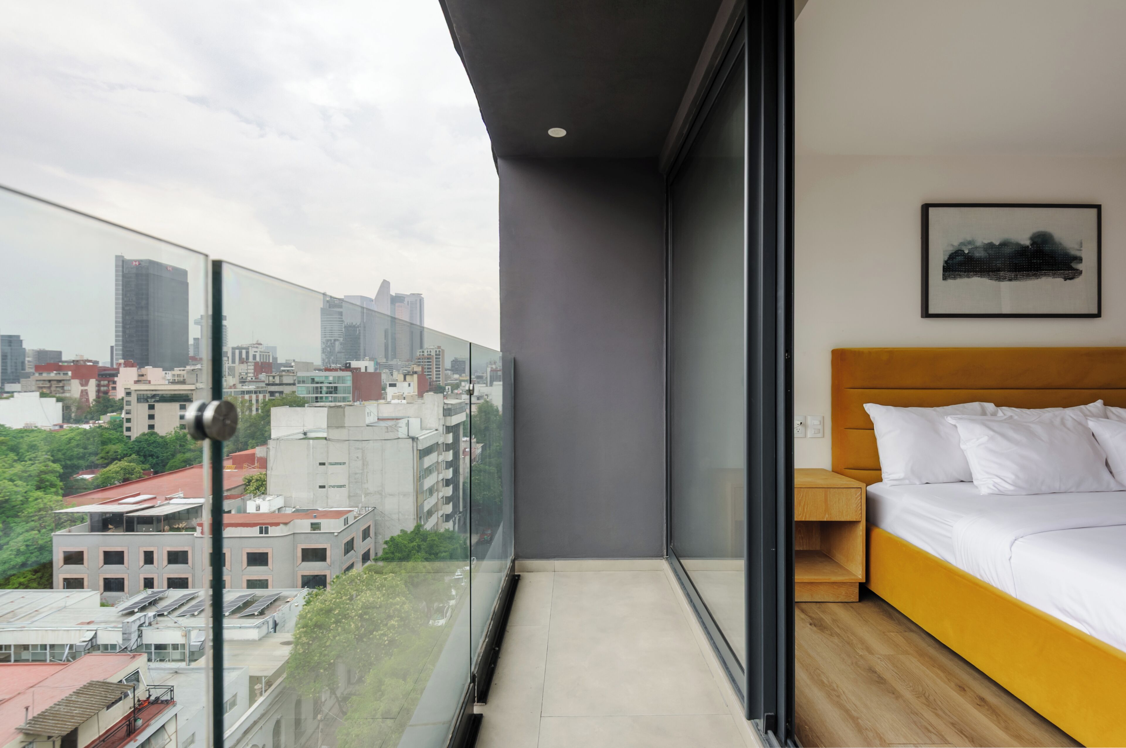 A modern bedroom with a city view, a bed with white bedding, and a wooden headboard.
