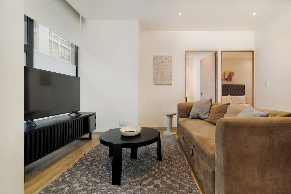 A modern living room with a flat-screen TV, a round coffee table, and a brown sofa.