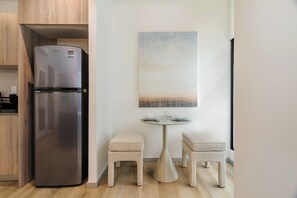 Una cocina moderna con un refrigerador de acero inoxidable, una pequeña mesa de comedor con dos taburetes y una obra de arte abstracta colgada en la pared.