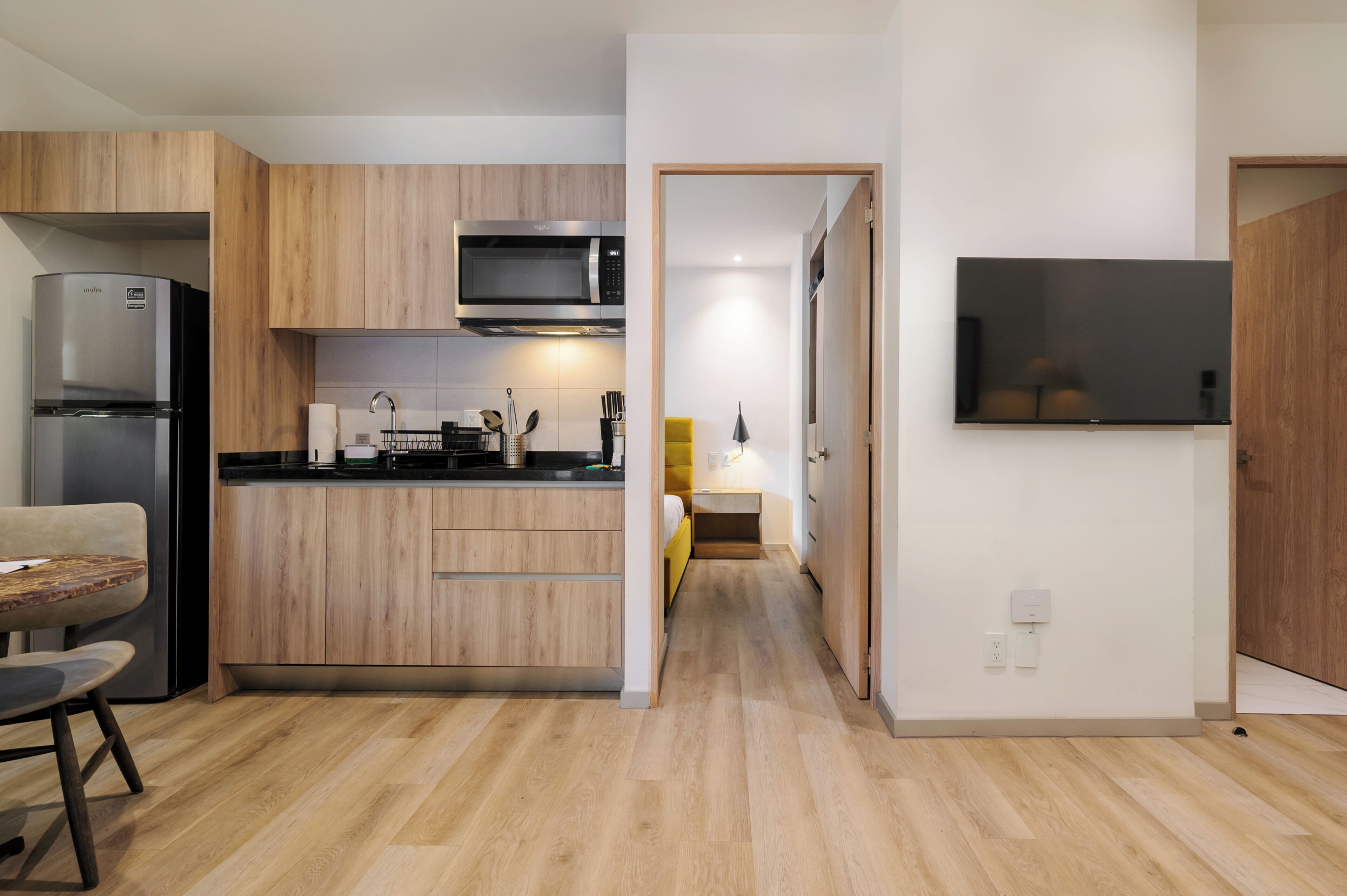 Una cocina moderna con armarios de madera, microondas integrado y un televisor de pantalla plana montado en la pared.