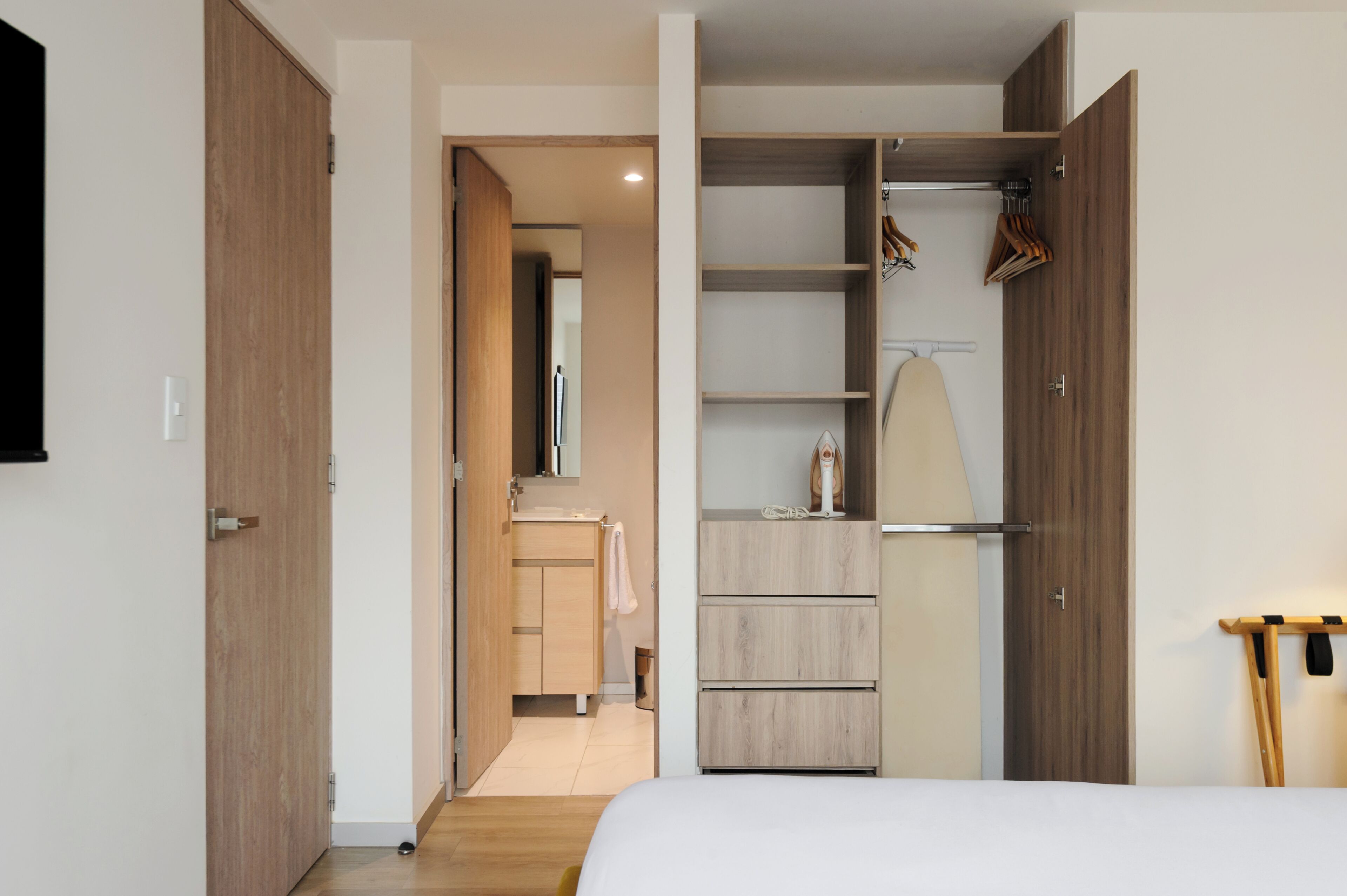 Un dormitorio con cama, armario, espejo y baño con lavabo y toalla.