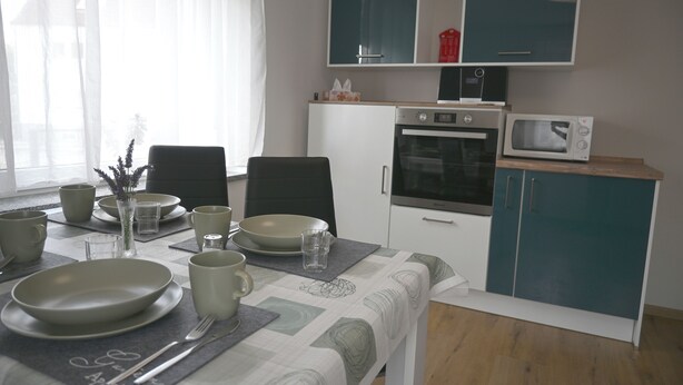 Een eethoek met een tafel voor vier personen, een magnetron, oven en kastjes in blauwgroen.