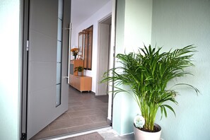 A hallway with a potted plant, a wooden cabinet with a vase of flowers, and a door leading to another room.