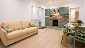 A modern apartment with a sofa, a dining table, a kitchen with a stove and oven, and a sliding door leading to a balcony. - Lemon Tree House con Piscina Privata Castelluzzo (San Vito Lo Capo)