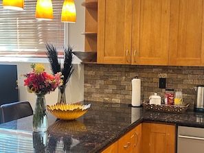 A kitchen with wooden cabinets, a black countertop, a vase with flowers, and a brick backsplash.