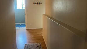 A hallway with a wooden floor, a rug, a coat rack, and a door leading to a bright room. - Serene 2-bedroom apartment in Tukwila perfect for your stay (Tukwila)