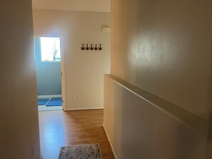 Ein Flur mit Holzboden, Teppich, Kleiderhaken und einer Tür zu einem hellen Raum.