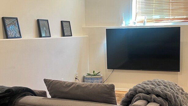 A living room with a sofa, a flat-screen TV mounted on the wall, and a small potted plant on a side table. - Serene 2-bedroom apartment in Tukwila perfect for your stay (Tukwila)