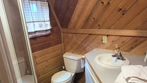 Et lille badeværelse i en træhytte med toilet, vask og bruser.
