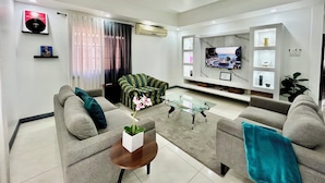 A modern living room with a flat-screen TV, grey sofas, a glass coffee table, and a decorative plant. - Enzo’s Suite Escape | Stylish 1BR in Liguanea (Kingston)