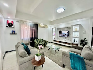 Ein modernes Wohnzimmer mit Fernseher, grauen Sofas, einem Glastisch und einer Zimmerpflanze.
