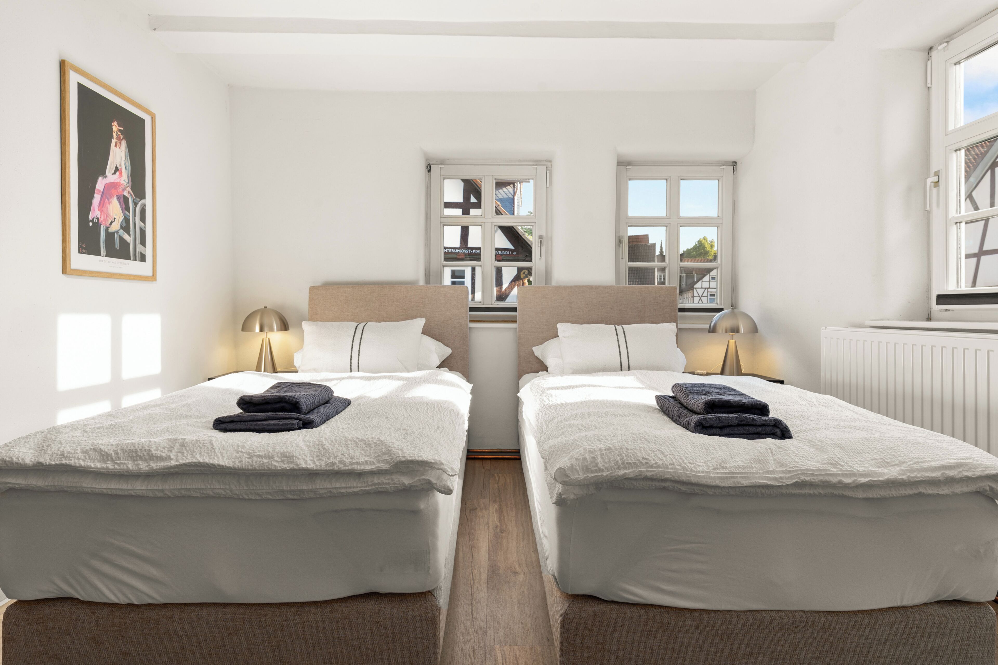 A hotel room with two beds, a framed picture on the wall, and a window with a view of buildings.