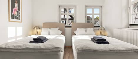 A hotel room with two beds, a framed picture on the wall, and a window with a view of buildings.