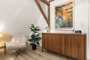 Un interior modern amb sostre de fusta, una obra d'art emmarcada d'un llac, una planta en test, una zona de seients i un armari de fusta.