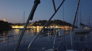 Een jachthaven met aangemeerde boten, rustig water en een stadsbeeld met lichtjes op de achtergrond.