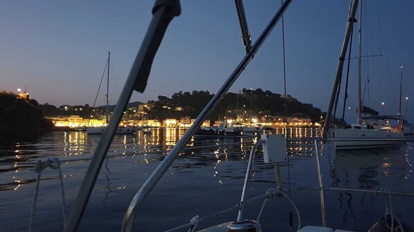 A marina with boats docked, calm water, and a cityscape with lights in the background.