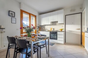 A modern kitchen with white cabinets, a dining table with chairs, and a window with curtains. - A Tuscan Gem | Family Home with 2 Gardens & Private Parking (Viareggio)