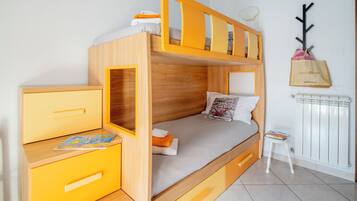 Una cama litera con escritorio y cajones, un radiador y un taburete pequeño.