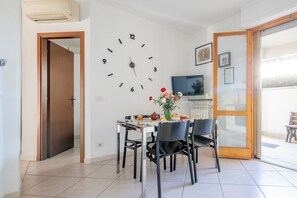 A dining area with a wall clock, a table set for two, and a television in the background. - A Tuscan Gem | Family Home with 2 Gardens & Private Parking (Viareggio)