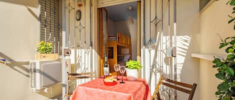 A small outdoor patio with a table set for two, a chair, and a potted plant.