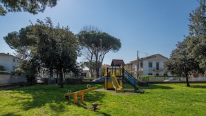 A playground with a slide and swings in a grassy area with trees and houses in the background. - A Tuscan Gem | Family Home with 2 Gardens & Private Parking (Viareggio)