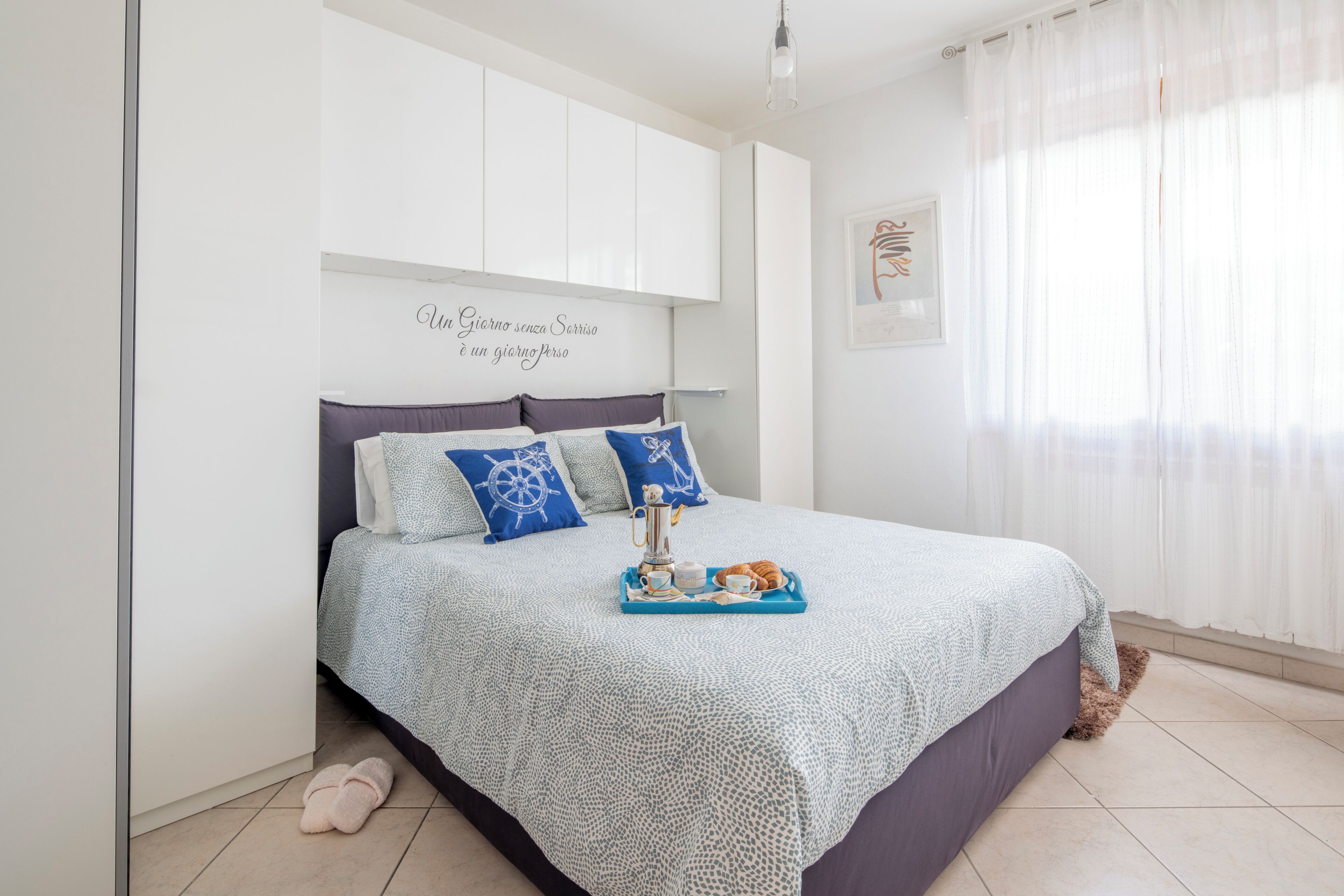 Ein Schlafzimmer mit einem Bett, einer Wandablage, einem gerahmten Zitat und einem Fenster mit Vorhängen.