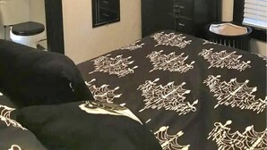 Een slaapkamer met een bed, een dressoir, een televisietoestel, een klok en een raam met jaloezieën.