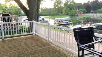 A wooden deck with a white railing, a black chair, and a view of a lake with boats and a dock.
