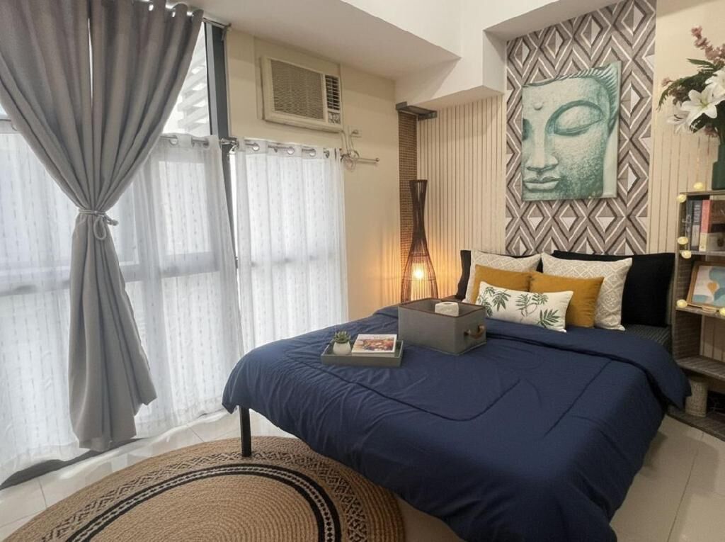 Un dormitorio con cama, cortinas, aire acondicionado de pared, mesita de noche con lámpara y un adorno en la pared.