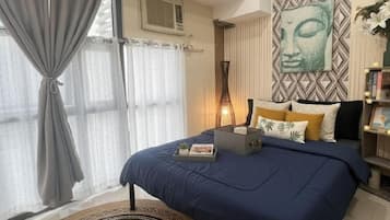 Un dormitorio con cama, cortinas, aire acondicionado de pared, mesita de noche con lámpara y un adorno en la pared.