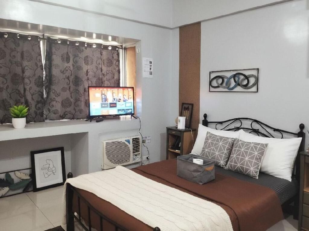 Een slaapkamer met een bed, een televisie, een radiator, een raam met gordijnen en een kunstwerk aan de muur.