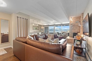 A modern living room with a brown leather sofa, a fireplace, and a large window overlooking a snowy landscape. - Lake and Lift Retreat: Your All-Season Escape (Dillon)